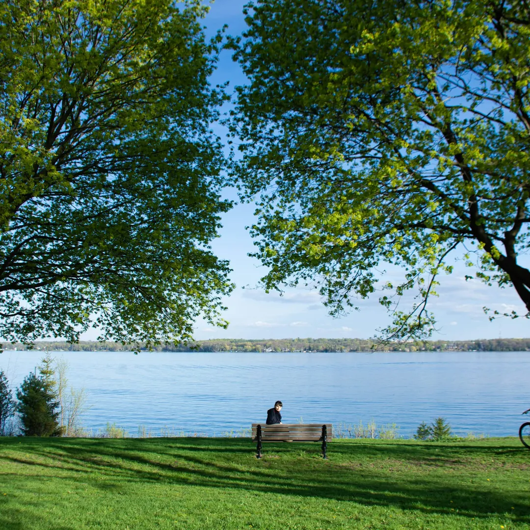 A bench under the trees in Kempenfelt Park, looking out over Kempenfelt Bay in Barrie